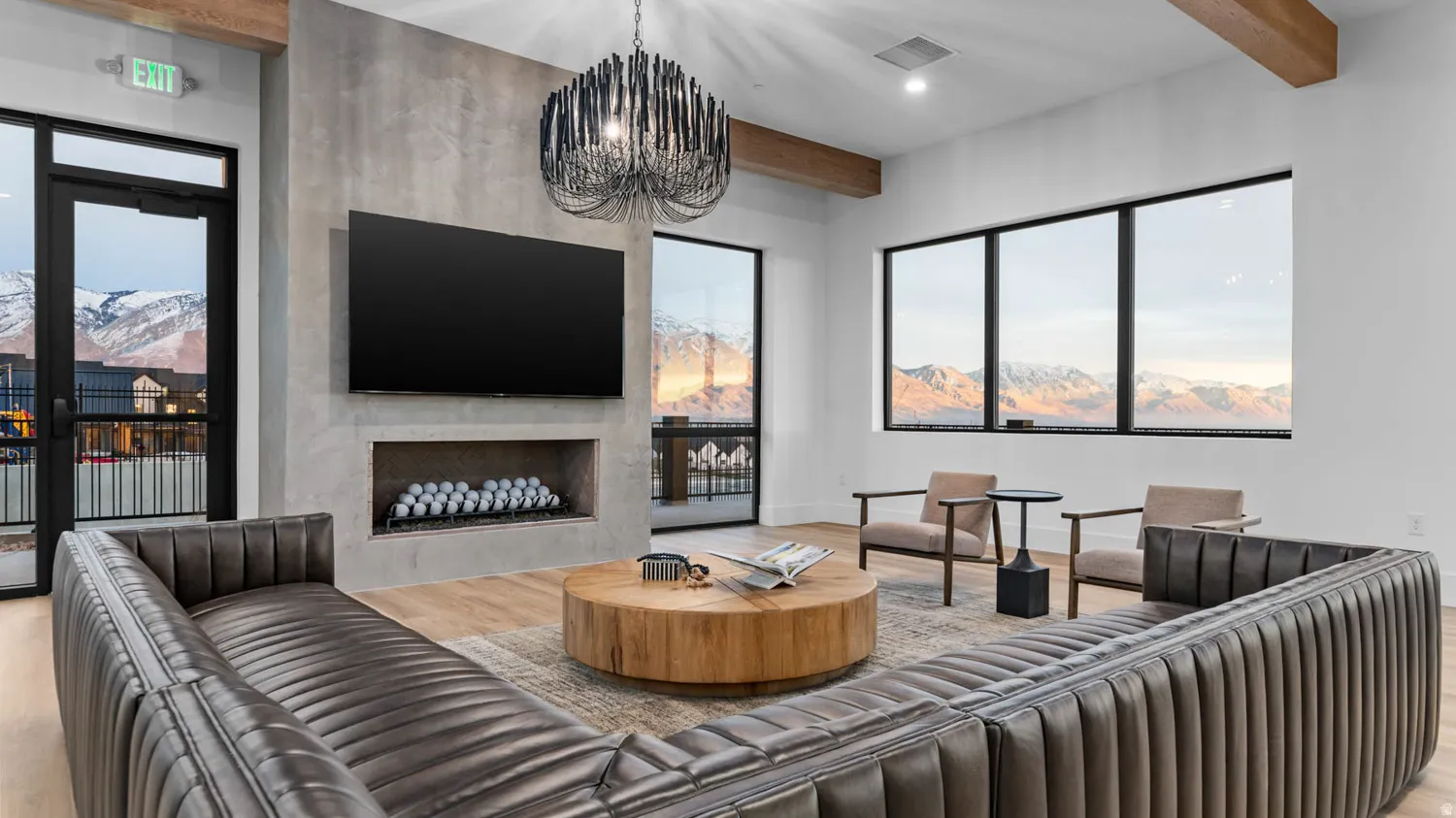 Spacious room featuring wood-finish flooring, a built-in fireplace with a television recess, exposed ceiling beams, and large picture windows