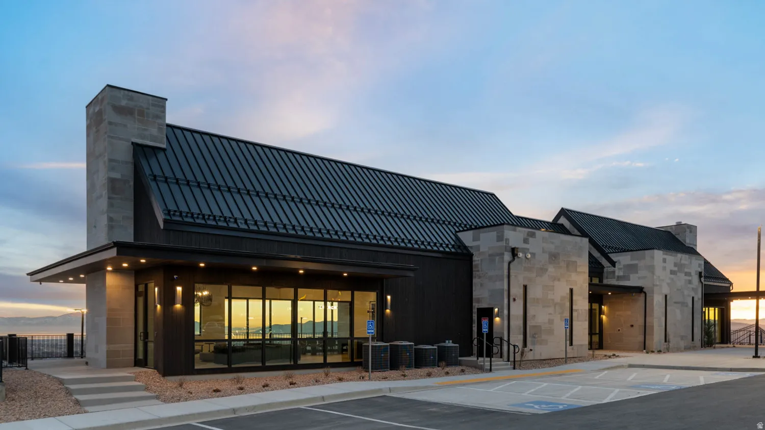 Modern architectural design featuring a standing seam metal roof, stone facade, expansive glass window walls, and exterior lighting