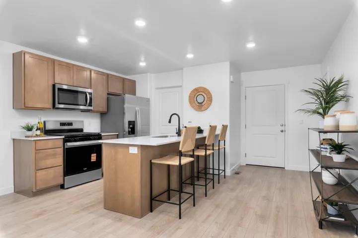 Modern kitchen featuring wood-finish cabinetry, stainless steel appliances, white countertops, and an island with a built-in sink