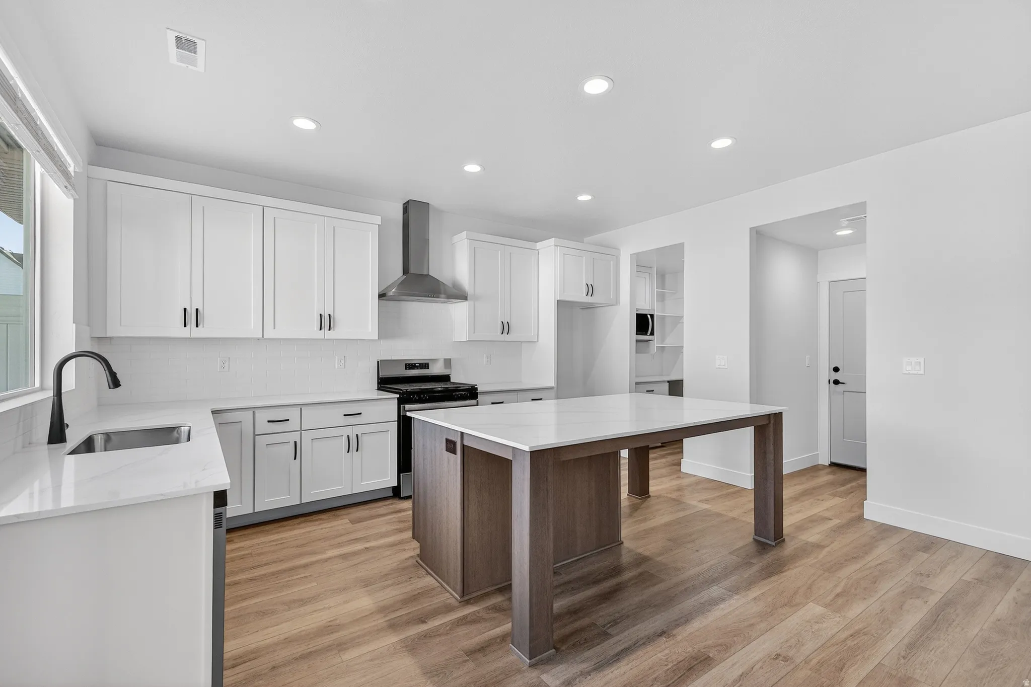 White shaker cabinetry, recessed lighting, wood-finish flooring, central island with solid surface countertop, and stainless steel appliances