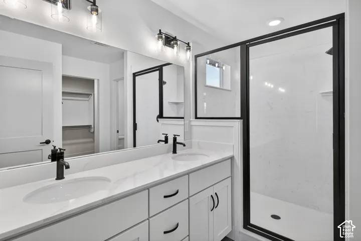 Dual vanity with integrated sinks, matte black fixtures, quartz countertops, white cabinetry, and a walk-in shower with black-framed glass enclosure