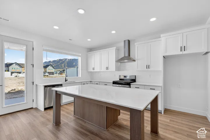 Kitchen featuring white shaker cabinetry, stainless steel appliances, wood-finish flooring, and a central island with a light-toned countertop