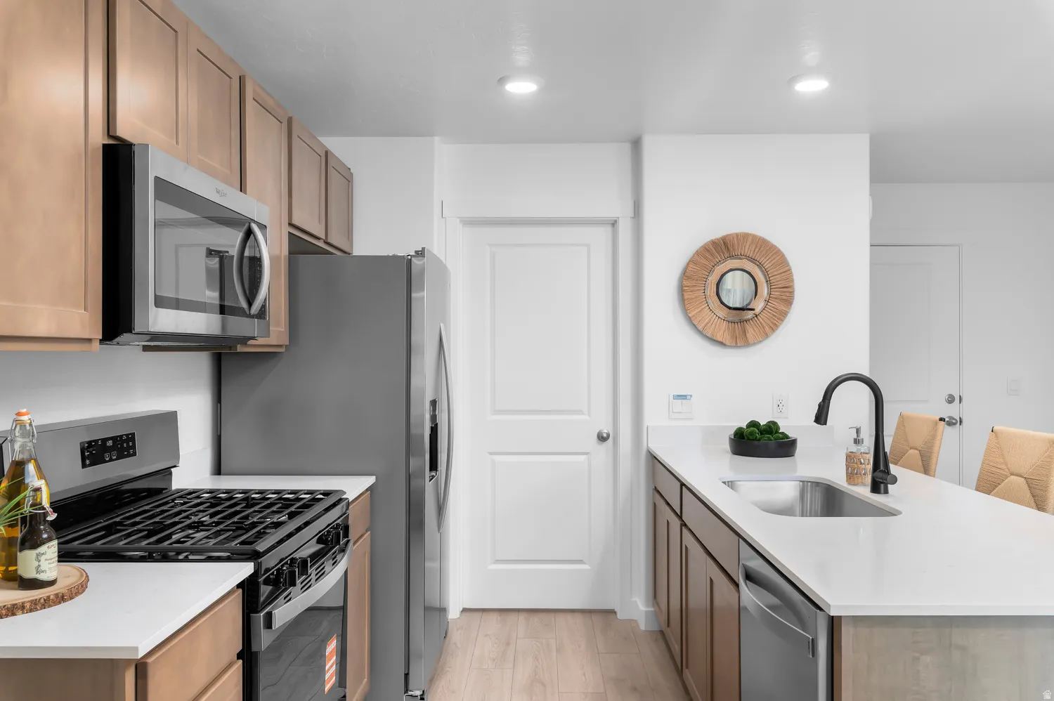 Kitchen featuring light wood-finish cabinetry, stainless steel appliances, solid surface countertops, a stainless steel sink, and a black gooseneck faucet