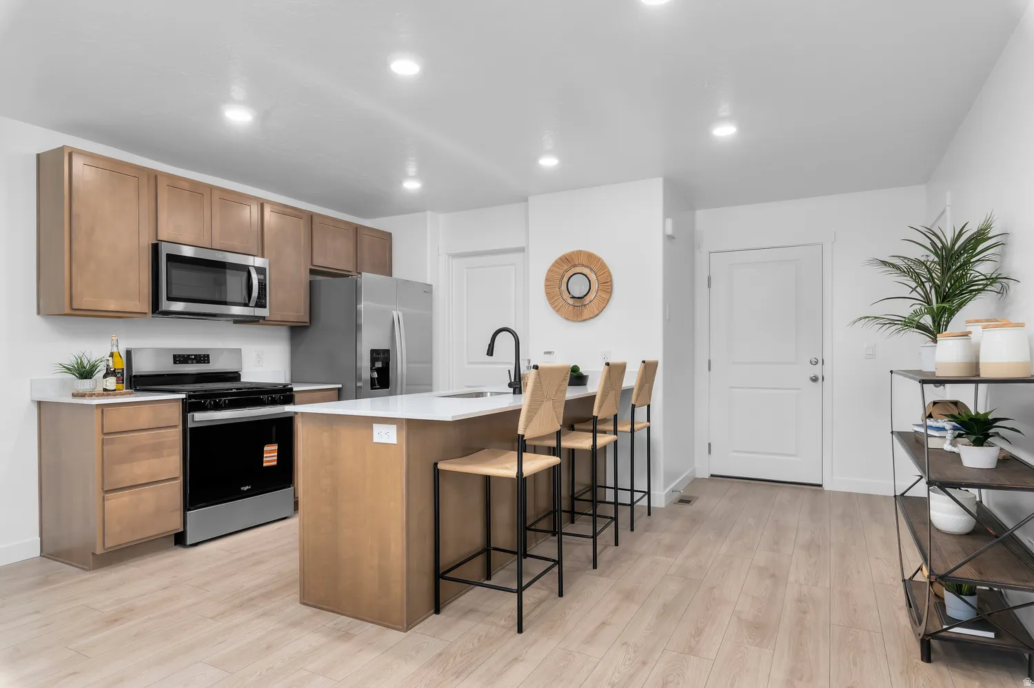 Kitchen featuring stainless steel appliances, wood-finish cabinetry, white countertops, a central island with a sink, and wood-finish flooring