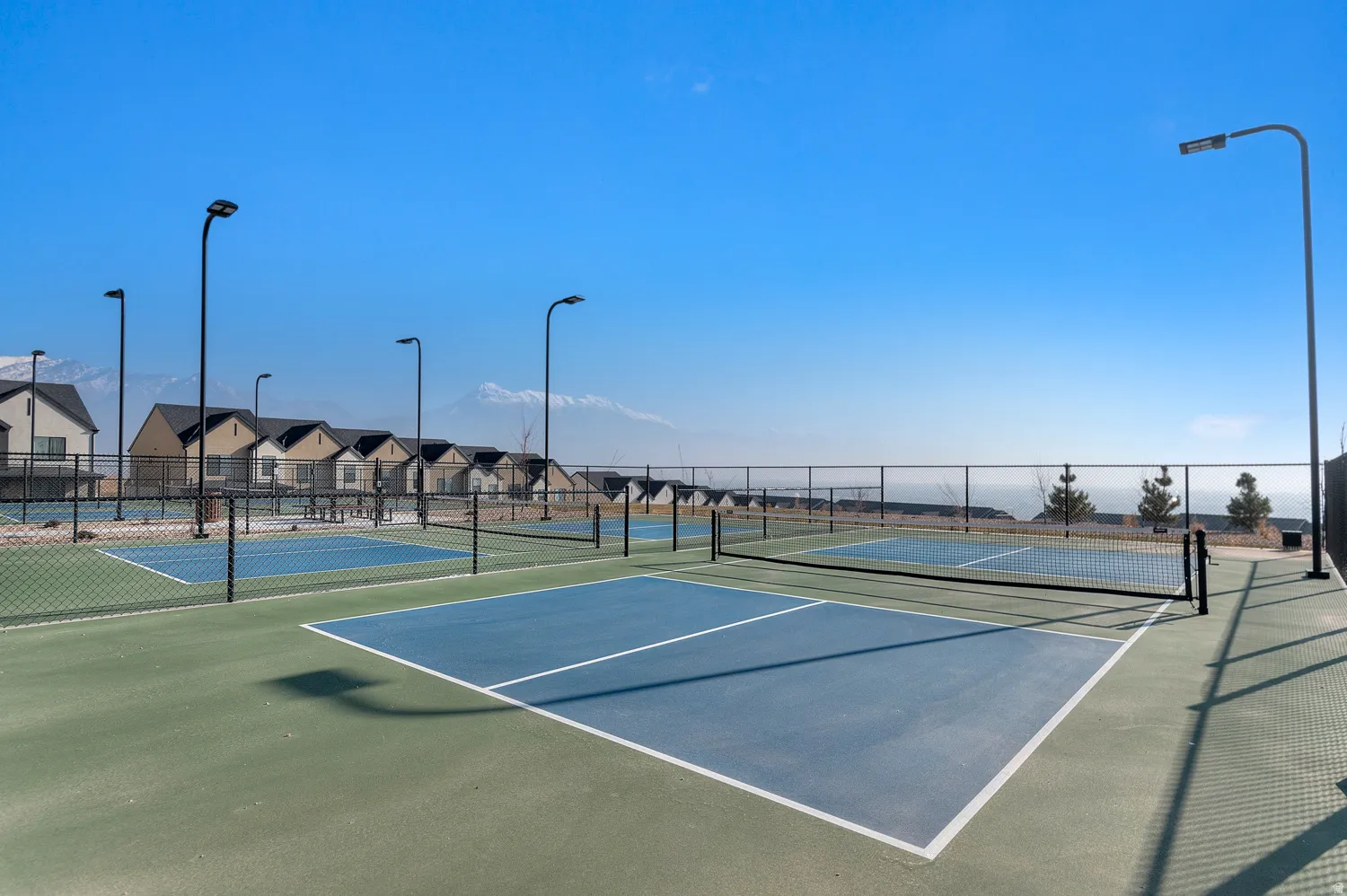 Multiple pickleball courts with perimeter fencing and light posts