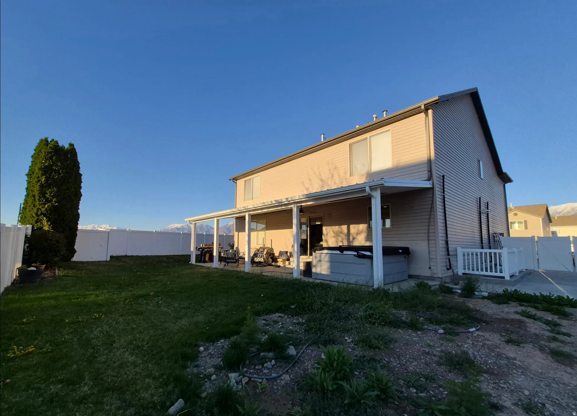 Expansive backyard featuring a covered patio, vinyl fencing, and a spa