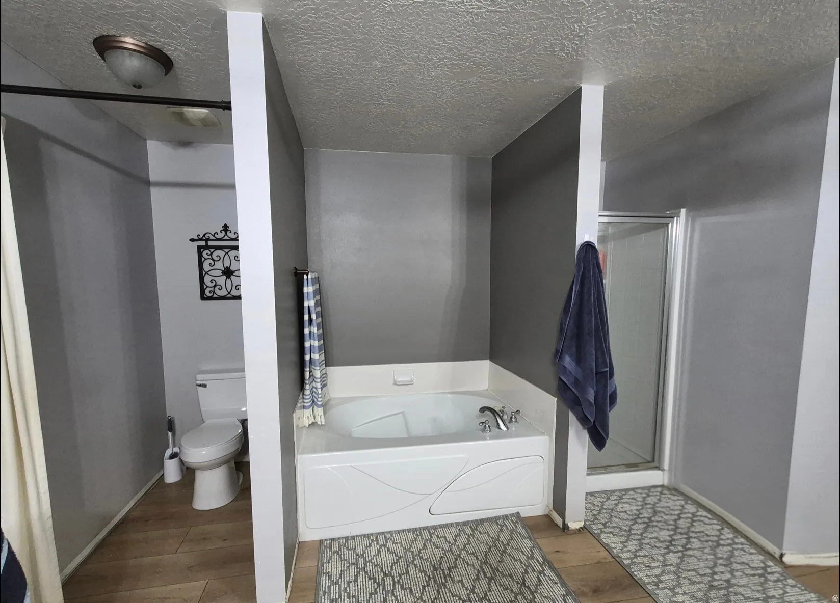 Soaking tub with chrome fixtures, glass-enclosed shower, and wood-finish flooring