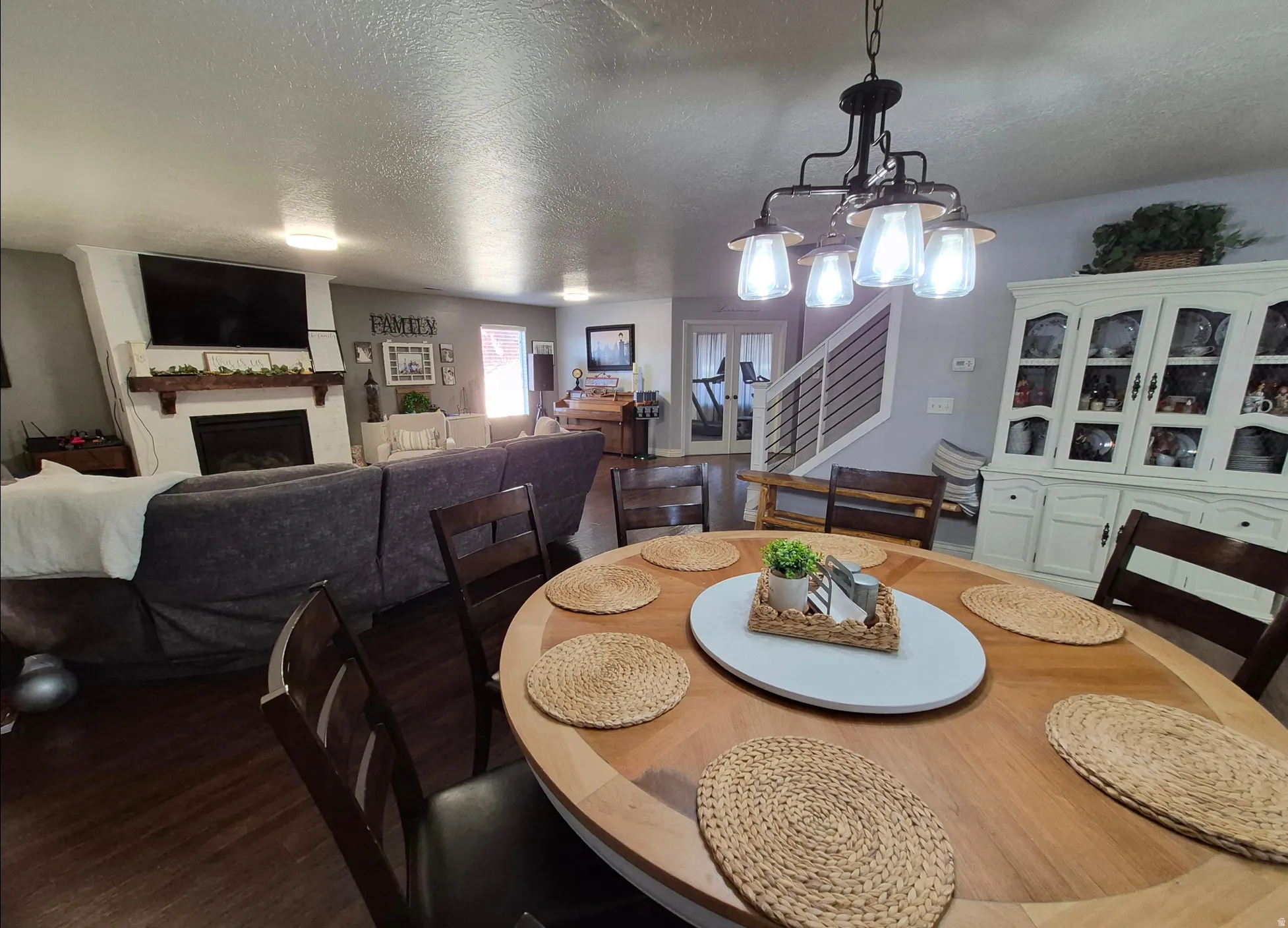 Wood-finish flooring throughout, a fireplace with a wood mantle, a white built-in hutch, a contemporary chandelier, and an open staircase with horizontal railings
