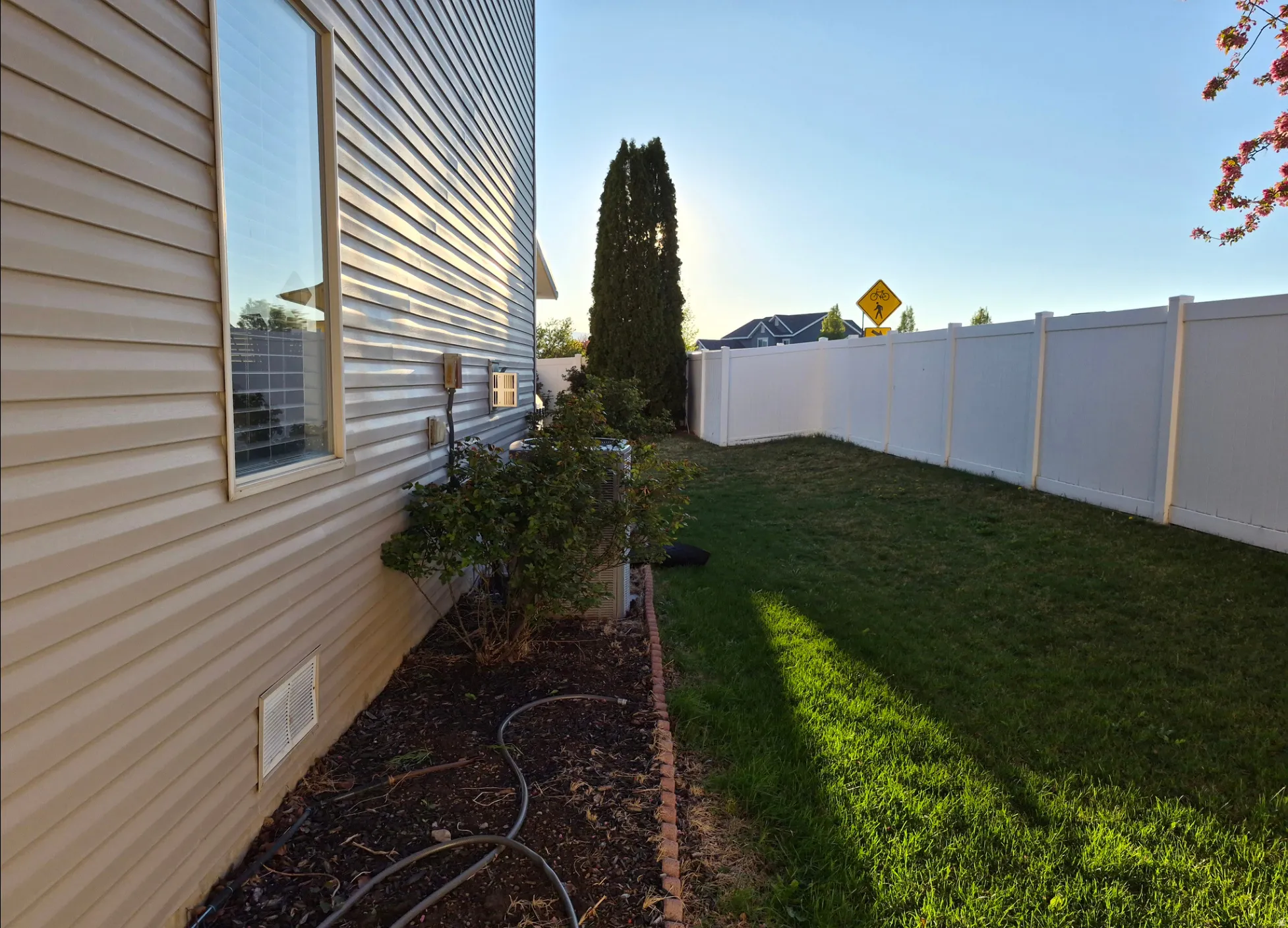Manicured lawn area with a white privacy fence and established landscaping