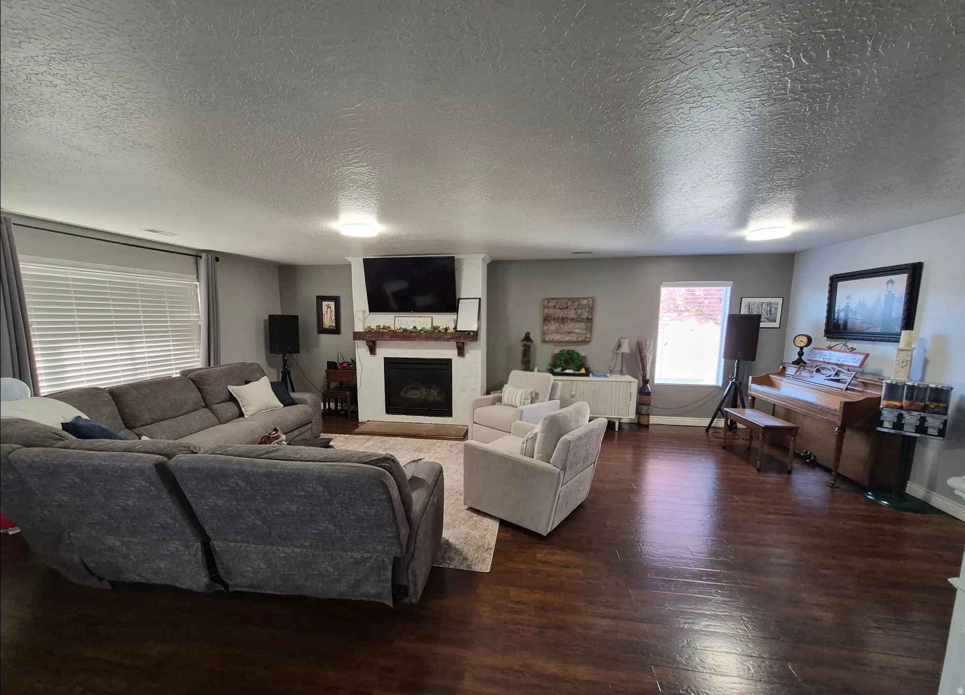 Spacious living area featuring wood-finish flooring, a white fireplace with a wood mantle, and recessed lighting