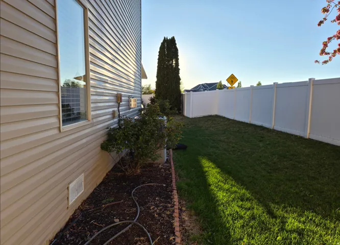 Manicured lawn area with a white privacy fence and established landscaping