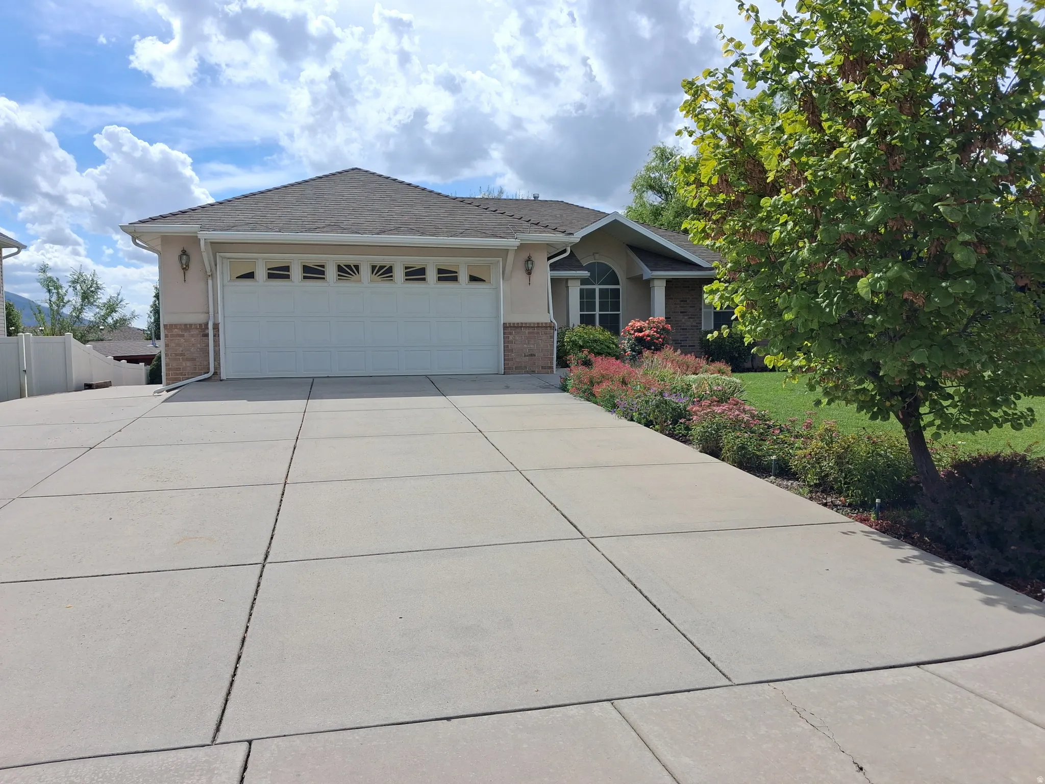 Concrete driveway, attached two-car garage with decorative windows, stucco and brick exterior, established landscaping, RV parking