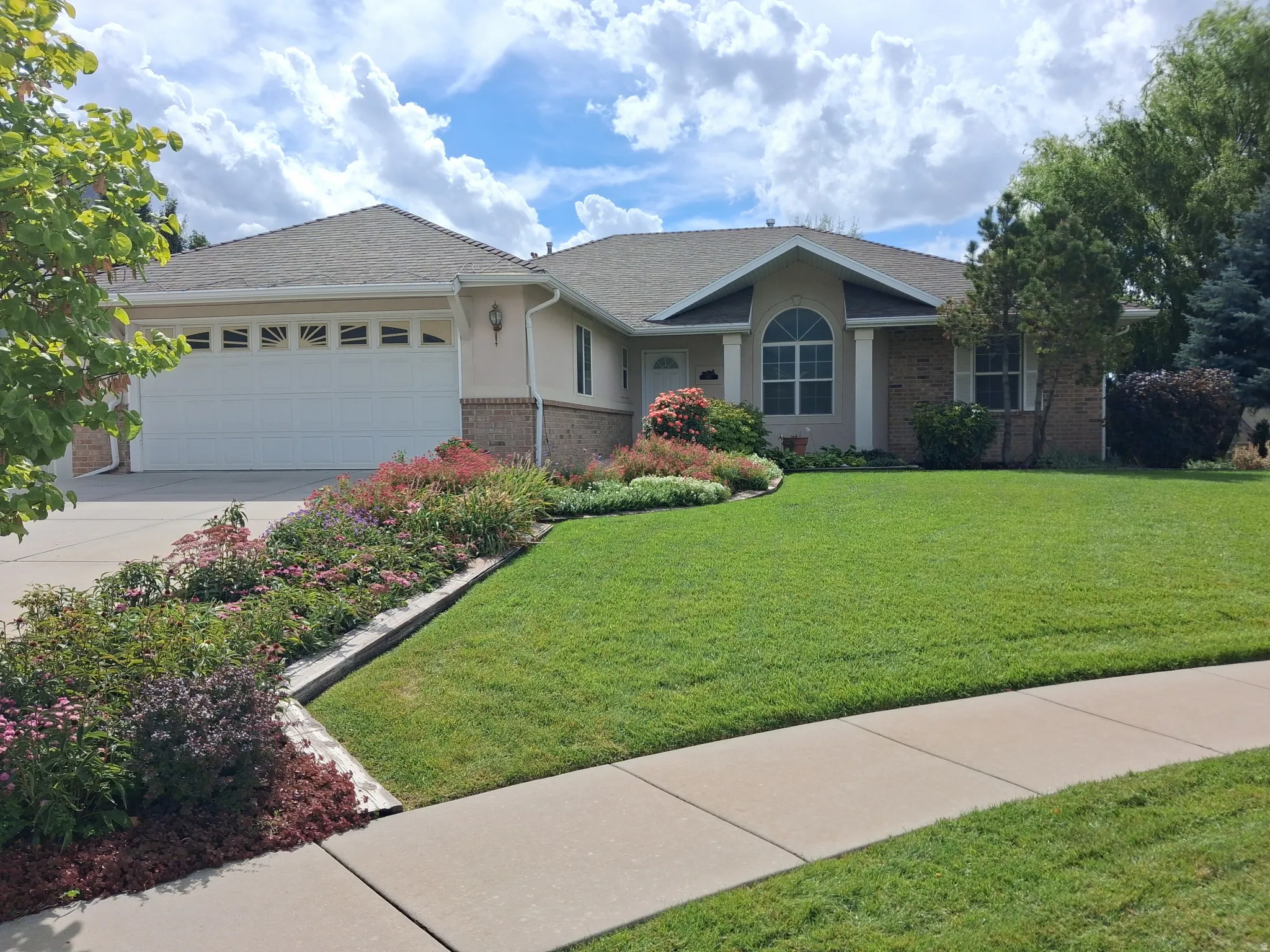 Single-story residence featuring a two-car garage with transom windows, brick and stucco exterior, and a well-maintained front lawn