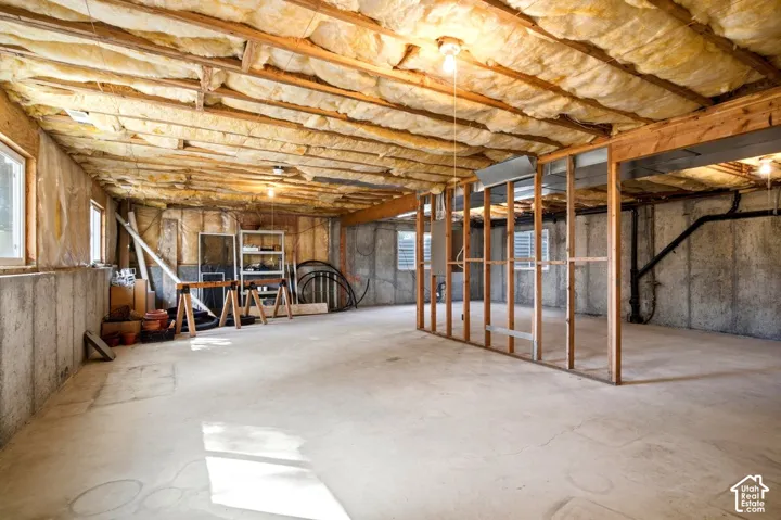 Unfinished basement with exposed concrete walls, wood framing, concrete flooring, and multiple windows for natural light