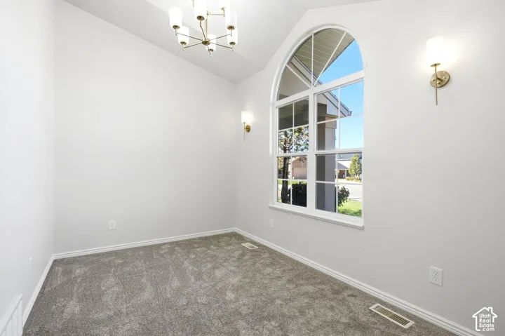 Arched window with clear glass, vaulted ceiling, grey carpet flooring, and a brass chandelier with frosted glass shades