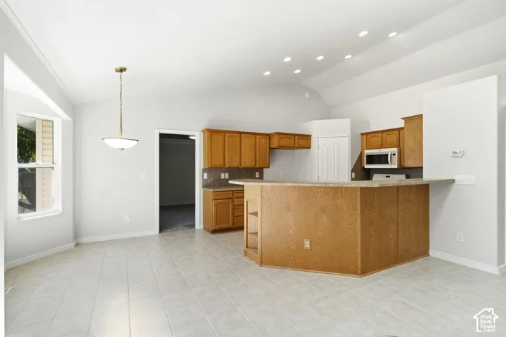 Open-concept kitchen and dining area featuring light wood cabinetry, stone-finish countertops, and a breakfast bar