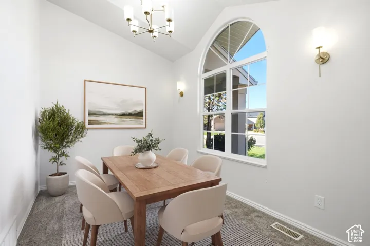 Arched window, vaulted ceiling, modern chandelier, wall sconces, and carpeting