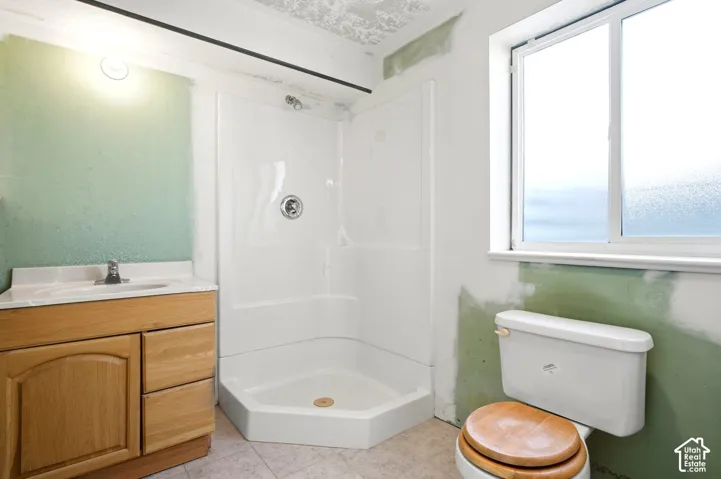 Partially finished basement bathroom, corner shower, single vanity with wood cabinetry, and a window with frosted panes