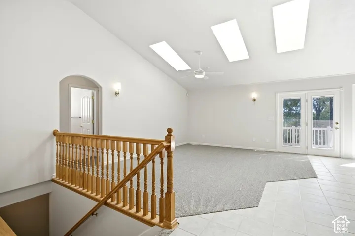 Vaulted ceiling with multiple skylights, ceiling fan, and double French doors opening to a balcony