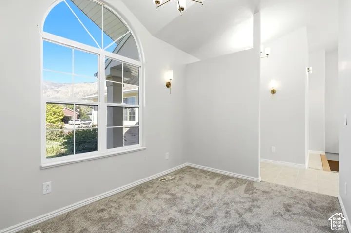 Arch-top window with multi-pane design, neutral wall paint, vaulted ceiling, brass wall sconces, and gray carpet flooring