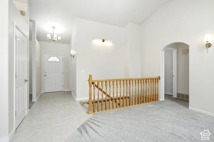 Arched hallway entry, wood spindle railing, chandelier lighting, and a white paneled door