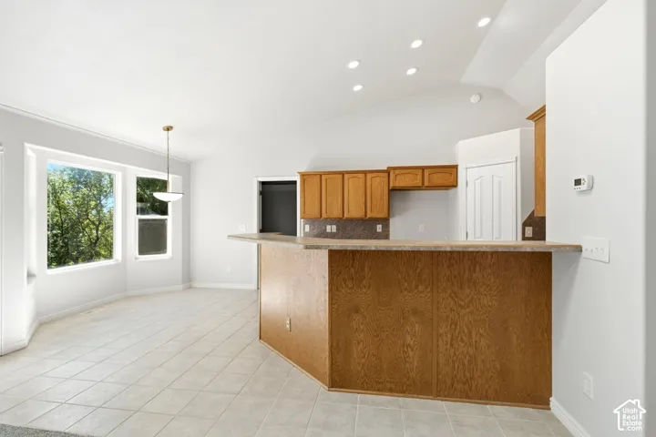 Vaulted ceilings with recessed lighting, tile flooring, wood-finish cabinetry, and a kitchen island with a breakfast bar