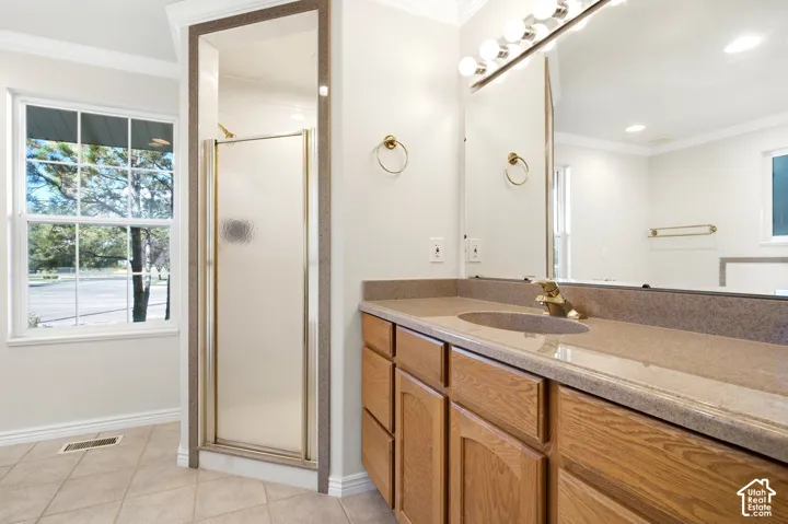 Primary bathroom with a wood-finish vanity with an integrated countertop, large vanity mirror, and an adjacent shower enclosure with a framed glass door
