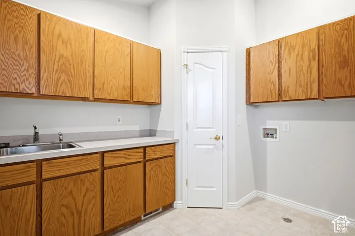 Light-toned wood cabinetry, stainless steel sink, light-colored countertops, tiled flooring, and a white paneled door