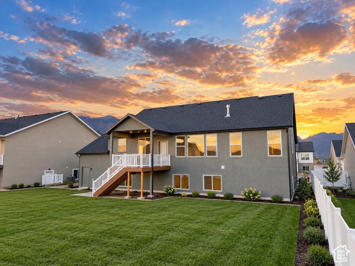 Expansive rear yard with a manicured lawn, elevated deck with staircase, and white picket fencing