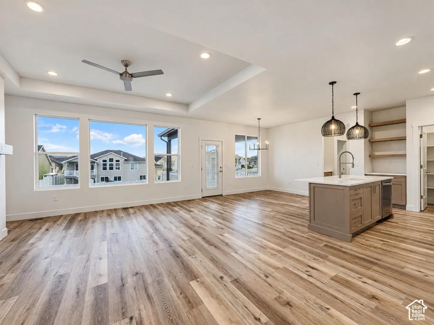 Tray ceiling with recessed lighting, wood-finish flooring, a kitchen island with sink and pendant lighting, and built-in shelving