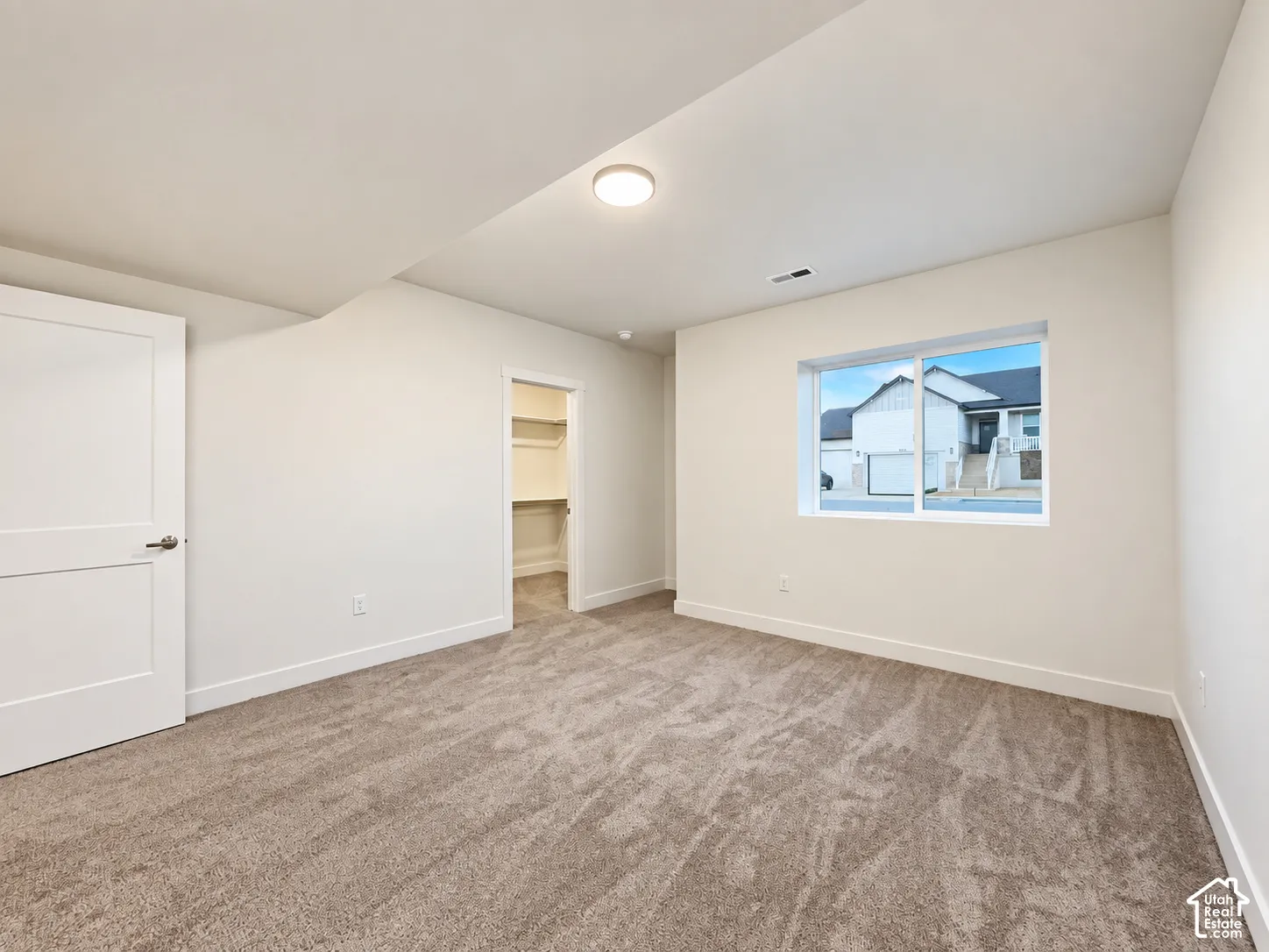 Carpeted flooring, white walls, built-in closet shelving, and a large window