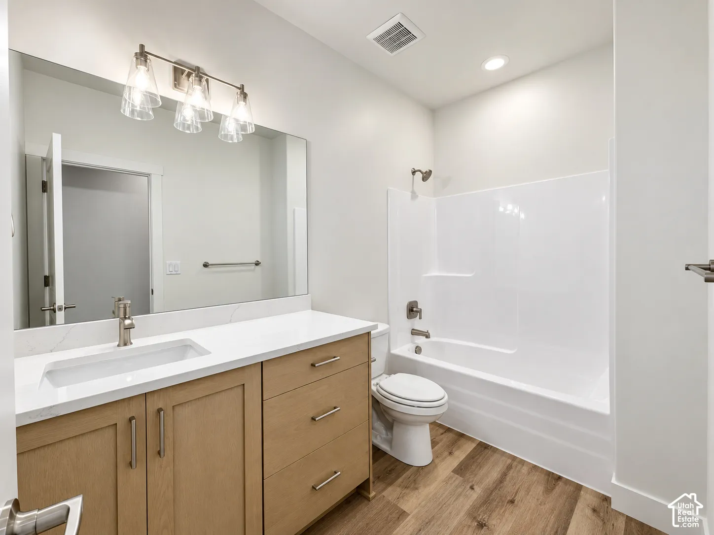 Wood-finish flooring, a contemporary vanity with an integrated rectangular sink, an expansive wall-mounted mirror, and a full bathtub with shower