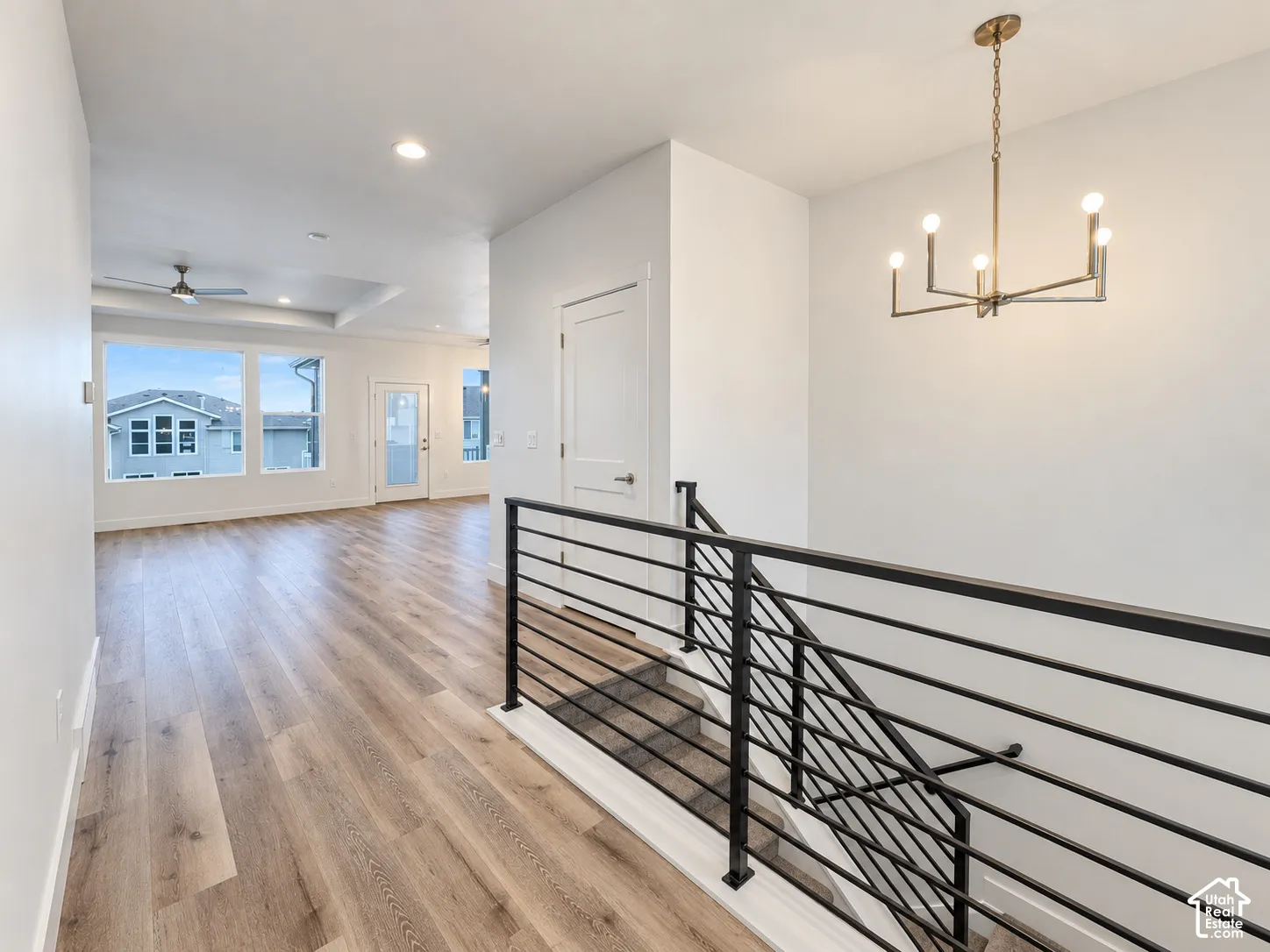 Wood-finish flooring throughout, modern black metal stair railing, contemporary brass-finish chandelier, recessed ceiling lighting, and large windows