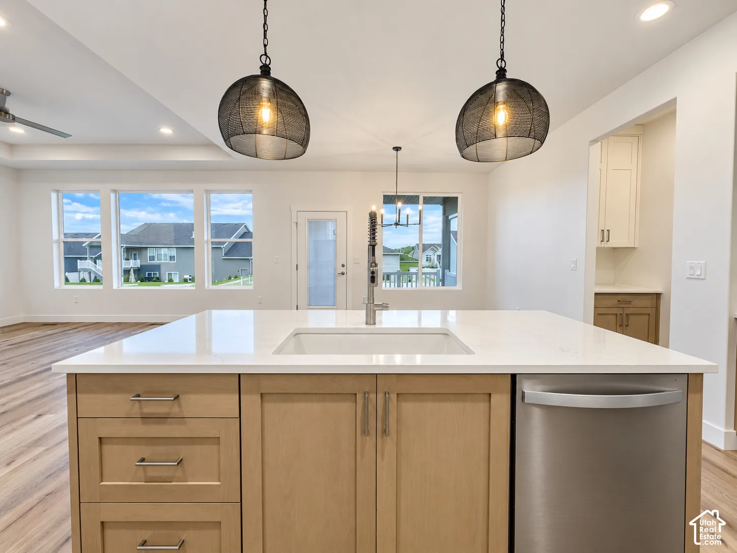 Kitchen island with an undermount sink, light wood-finish cabinetry, and stainless steel dishwasher