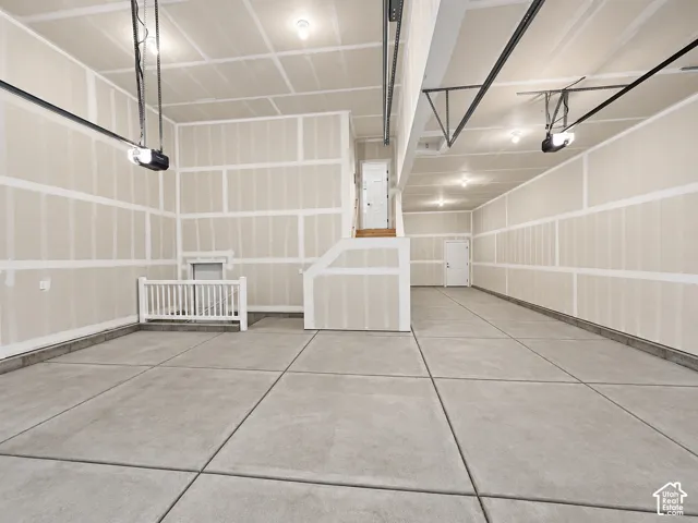 Expansive garage space featuring concrete flooring, unpainted drywall, recessed lighting, two garage door openers, and a finished staircase with wood treads