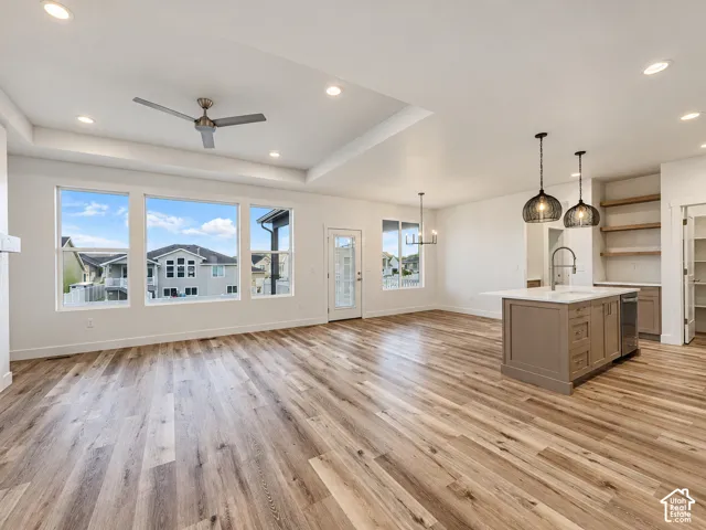 Tray ceiling with recessed lighting, wood-finish flooring, a kitchen island with sink and pendant lighting, and built-in shelving