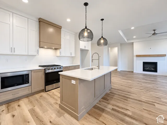 Kitchen featuring wood-finish flooring, two-tone cabinetry, stainless steel appliances, a center island with sink, and pendant lighting