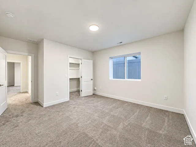 Spacious room featuring neutral carpeting, a dual-door closet with shelving, a large window, a ceiling-mounted light fixture, and white trim