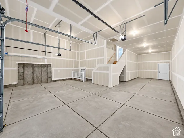 Concrete flooring, exposed block foundation, staircase with wood-finish treads, interior door, and garage door track system