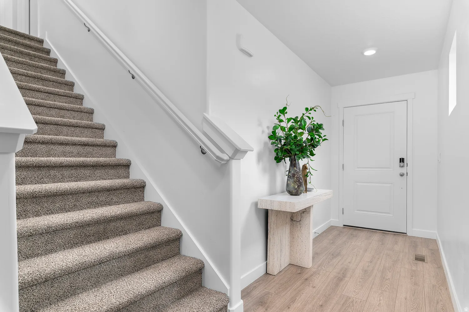 Carpeted staircase with white handrails, wood-finish flooring, and a solid entry door with smart lock hardware