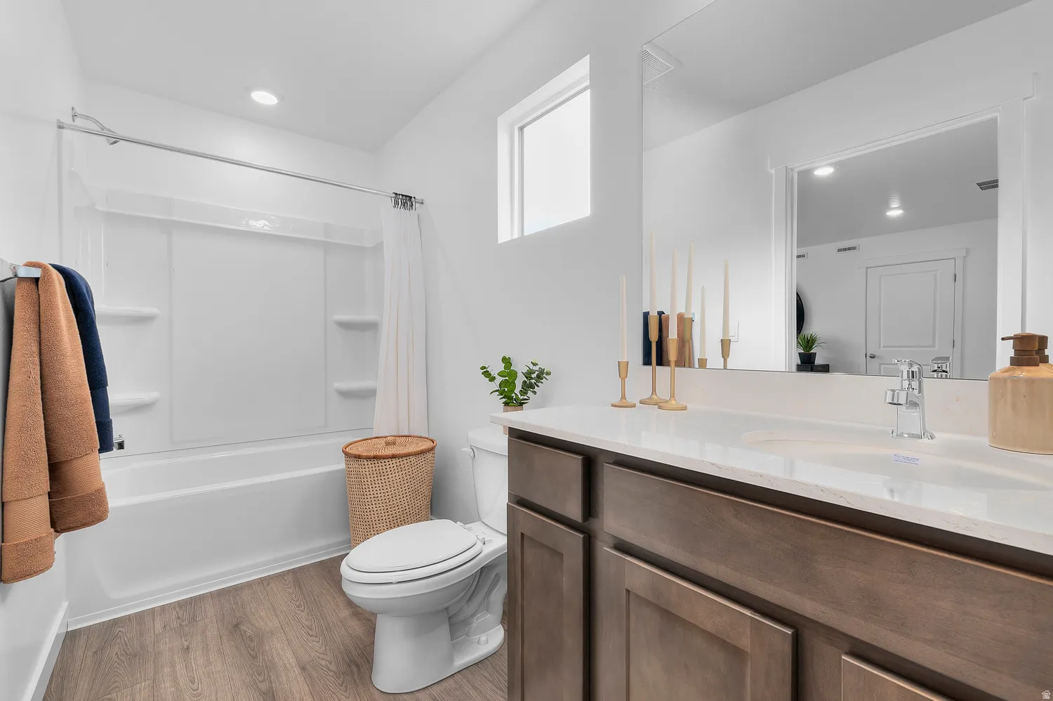 White bathtub and shower combination with integrated shelving, wood-finish flooring, dark wood vanity with integrated sink, light countertop, and wall-mounted mirror