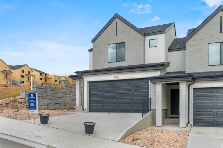 Modern stucco exterior with dark gray garage doors, a concrete driveway, and a stone retaining wall
