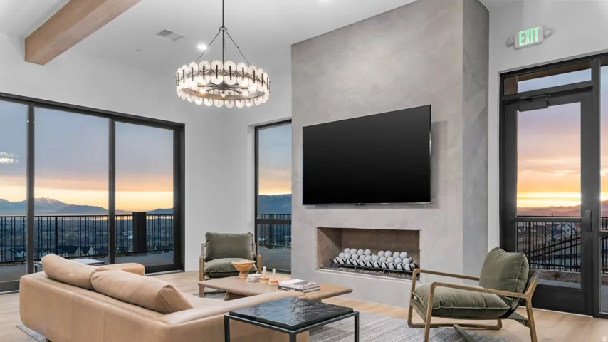 Expansive sliding glass doors, integrated linear fireplace, exposed beam ceiling, and a contemporary chandelier