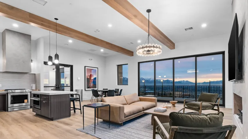 Expansive window wall with mountain backdrop, wood-finish flooring, exposed ceiling beams, built-in kitchen island, and stainless steel appliances