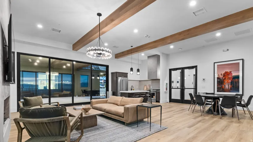 Spacious common area featuring wood-finish flooring, exposed beam ceiling, a modern chandelier, and a kitchen with stainless steel appliances and a range hood