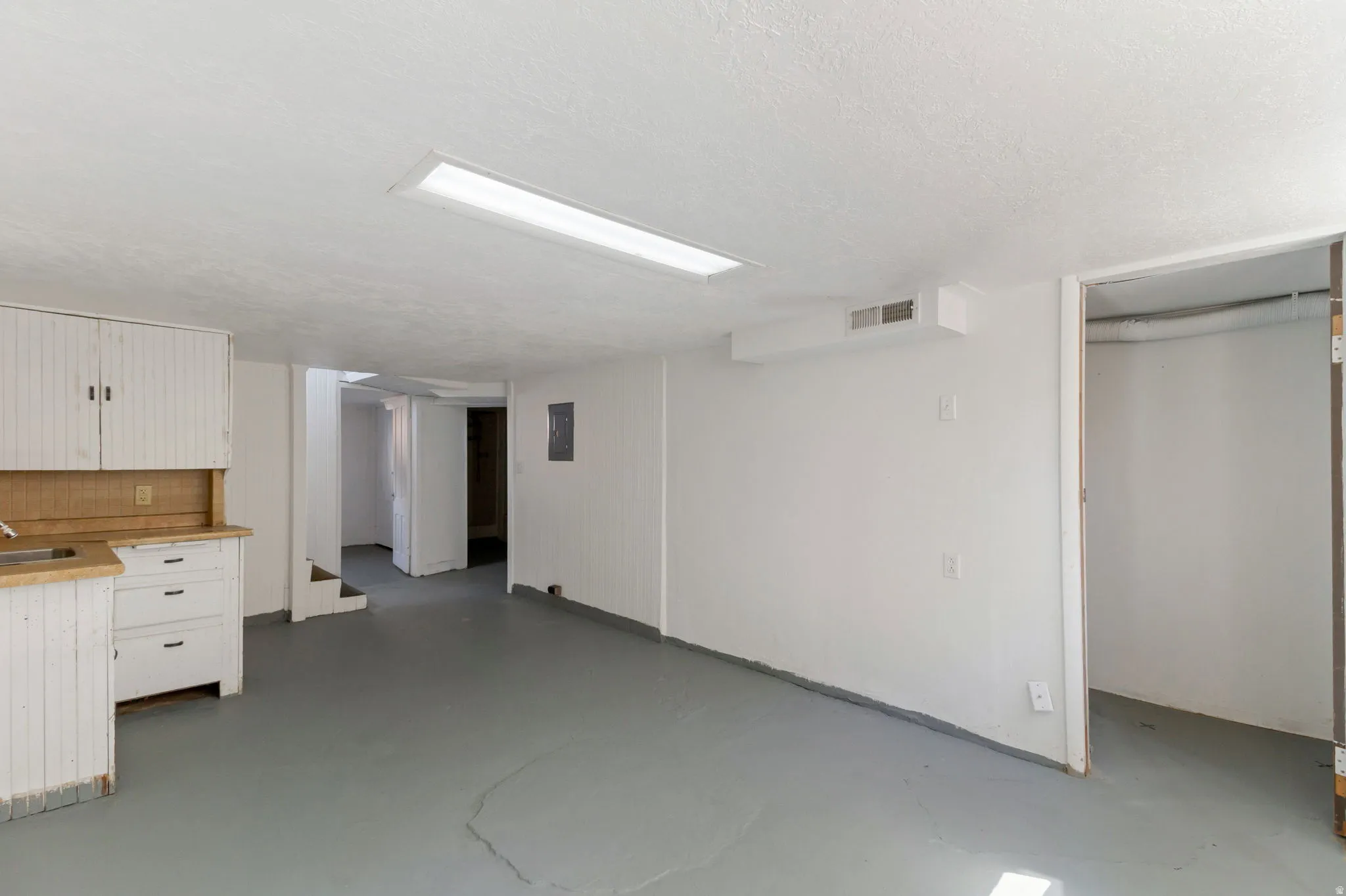 Spacious room featuring a utility sink, white cabinetry with wood-finish countertops, and a built-in overhead fluorescent light fixture