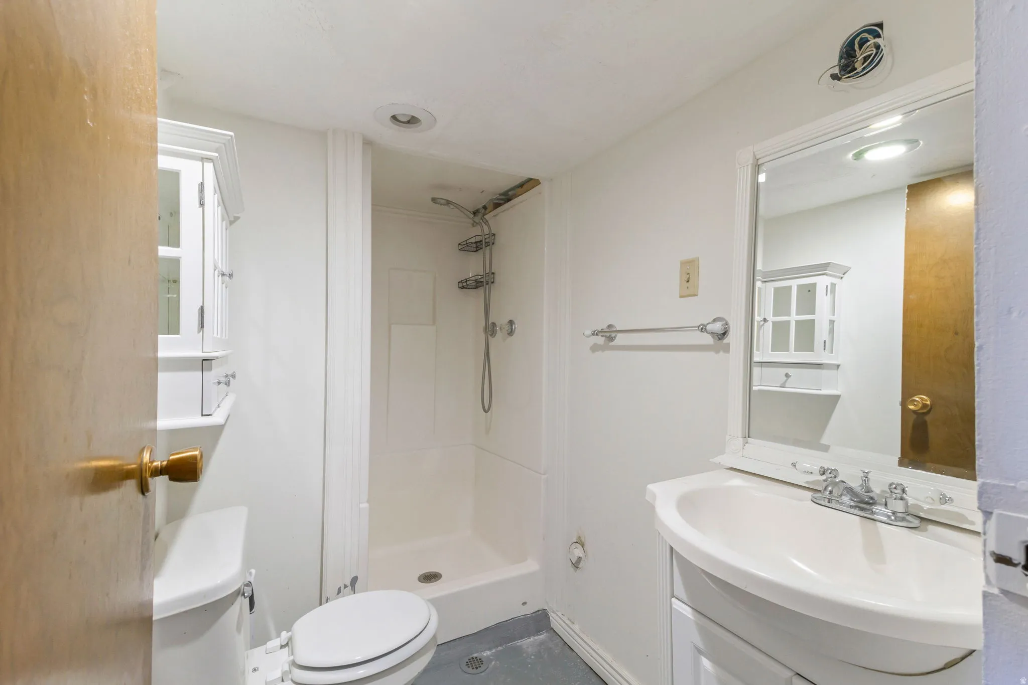 White vanity with integrated sink, wall-mounted mirror, stand-up shower, and built-in wall cabinet