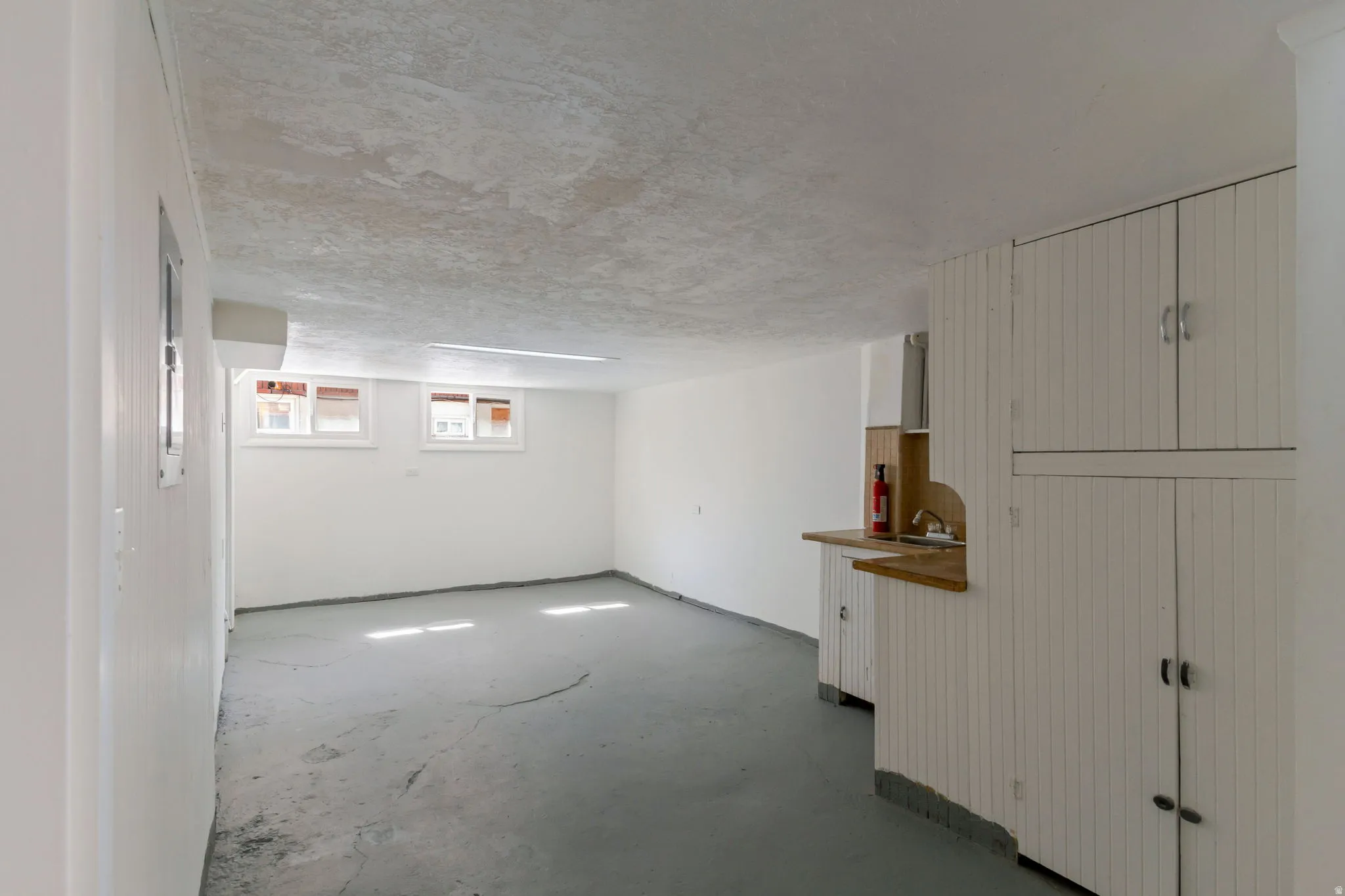 White painted walls, concrete flooring, built-in cabinetry with beadboard paneling, countertop with sink, and natural light from multiple windows