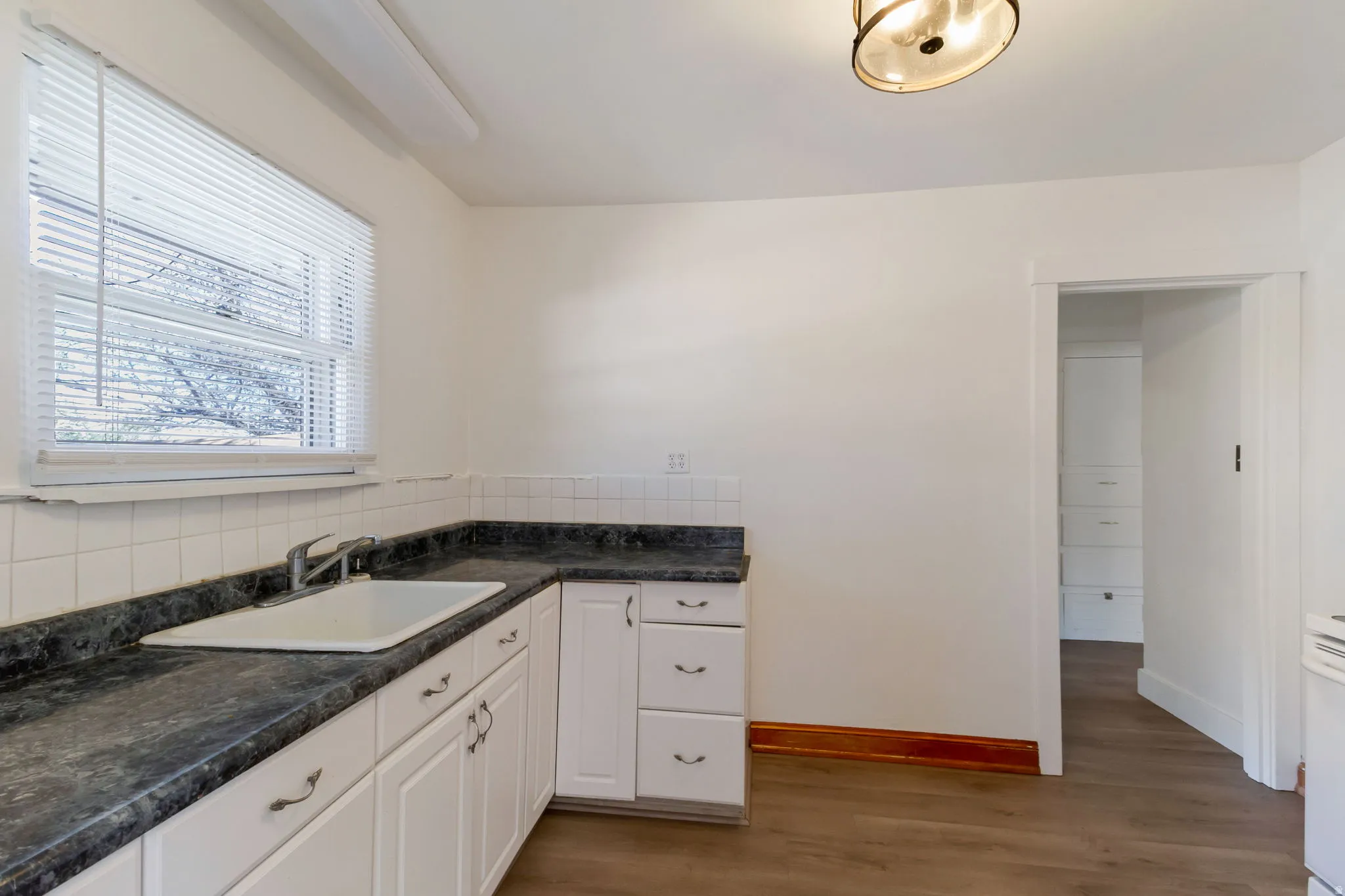 Kitchen featuring white cabinetry, dark countertops, a white tile backsplash, wood-finish flooring, and a ceiling-mounted light fixture