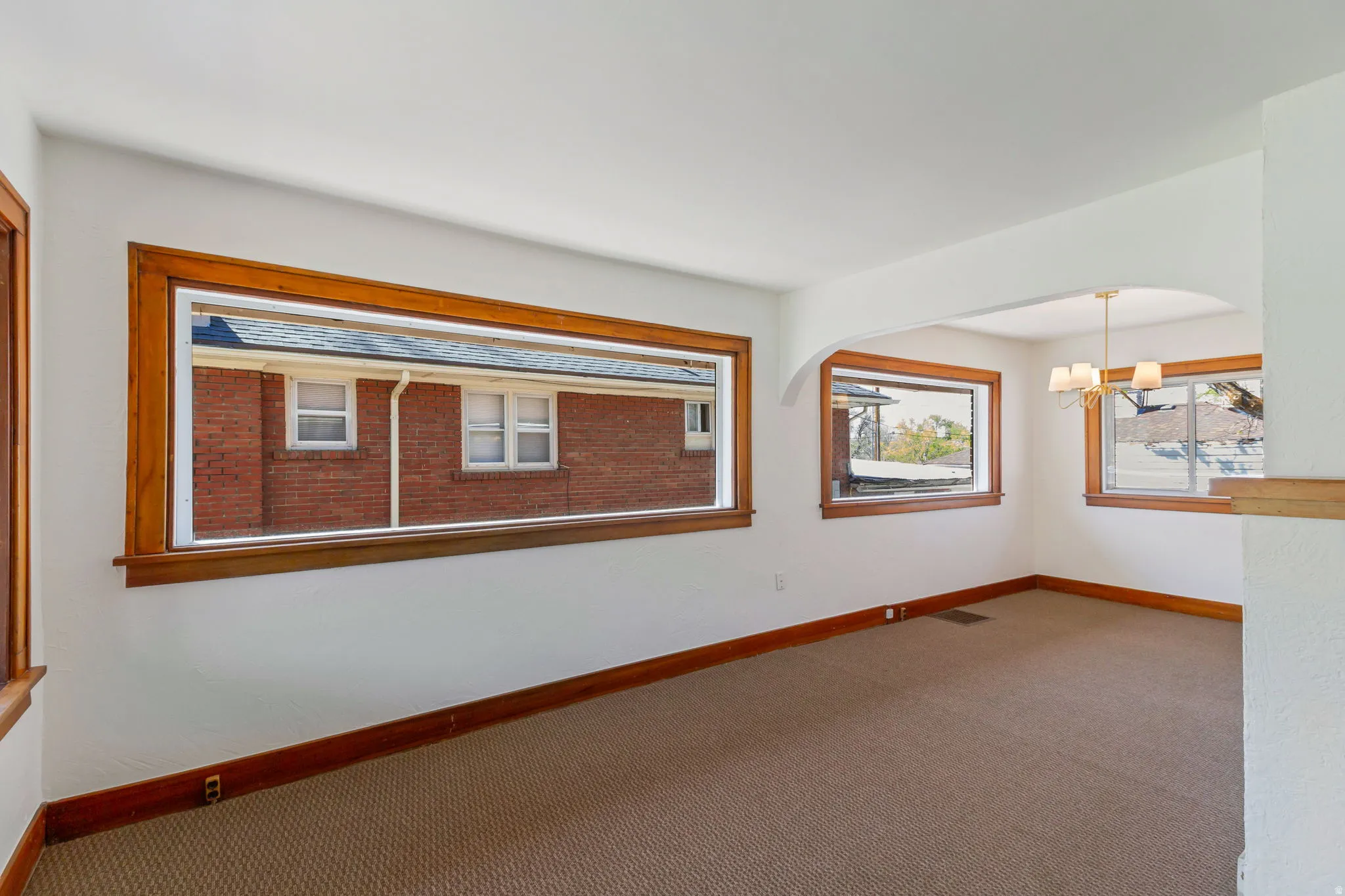 Expansive room featuring multiple windows with wood trim, neutral carpeting, and an arched entry to an adjacent space with a chandelier